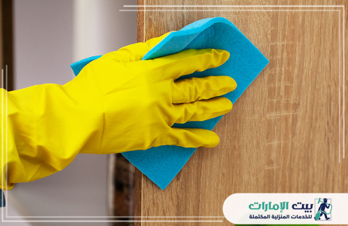 شركة تنظيف الكنب في أم القيوين لابد لـشركة تنظيف الكنب في أم القيوين أن تولي اهتمامًا بالأسطح المختلفة، تمامًا كما تُظهر الصورة يدًا ترتدي قفازًا أصفر وتمسح سطحًا خشبيًا بقطعة قماش زرقاء